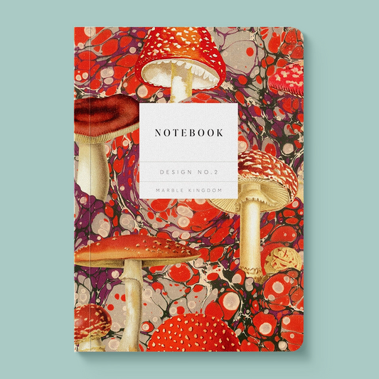A notebook with a vibrant, detailed cover illustration of red and white mushrooms over a red, purple, and black marbled pattern. The center of the cover features a white rectangular label with the text 'NOTEBOOK', 'DESIGN NO.2'