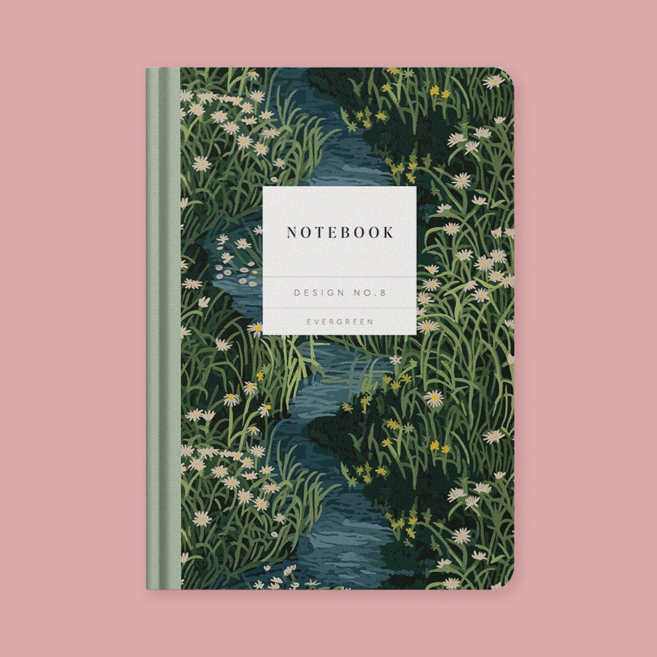 A notebook with a nature illustration cover featuring a winding blue stream surrounded by green grasses and white wildflowers, with a white label on the front reading 'NOTEBOOK', 'DESIGN NO.8', and 'EVERGREEN'.