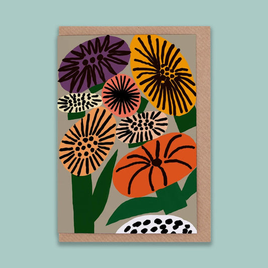 A portrait orientation greetings card with a digital illustration of colourful flowers on a beige background. The card is on a brown envelope on a plain backdrop. 