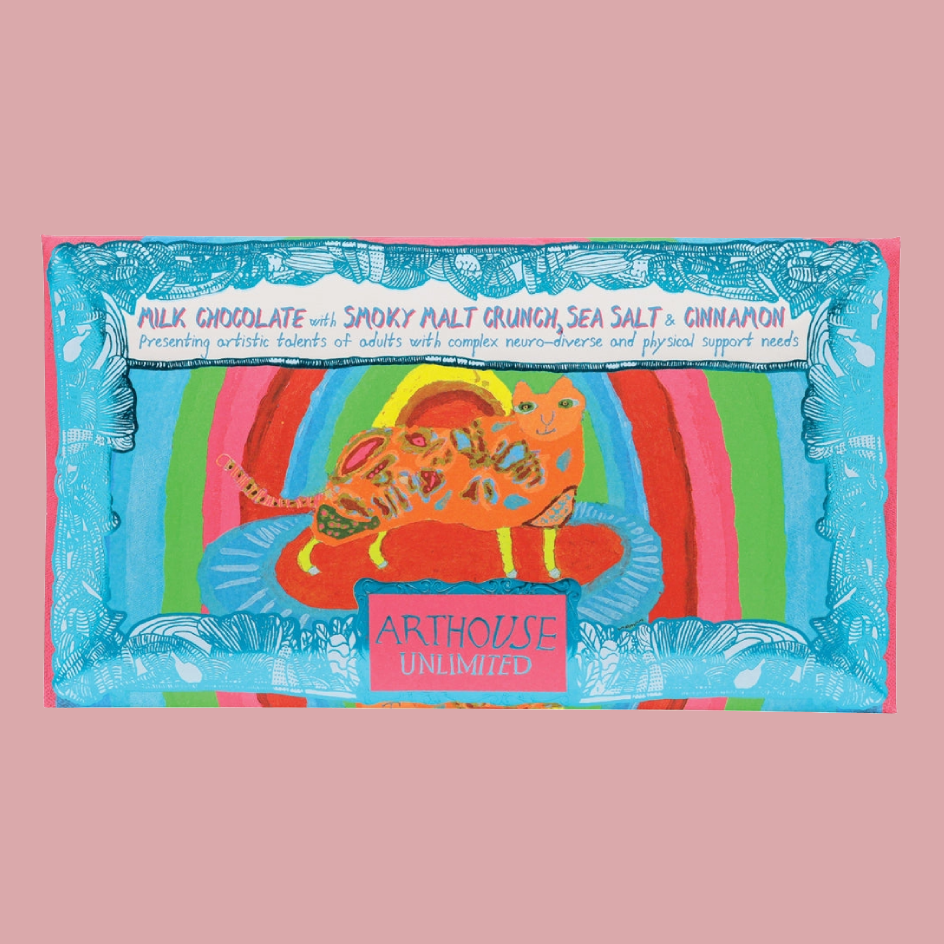 A colourful product package featuring a whimsical illustration of a cat in a striped environment, with text including 'MILK CHOCOLATE with SMOKY MALT CRUNCH, SEA SALT & CINNAMON' and 'ARTHOUSE UNLIMITED'. The item is centered on a solid pink background.