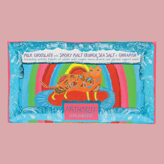 A colourful product package featuring a whimsical illustration of a cat in a striped environment, with text including 'MILK CHOCOLATE with SMOKY MALT CRUNCH, SEA SALT & CINNAMON' and 'ARTHOUSE UNLIMITED'. The item is centered on a solid pink background.