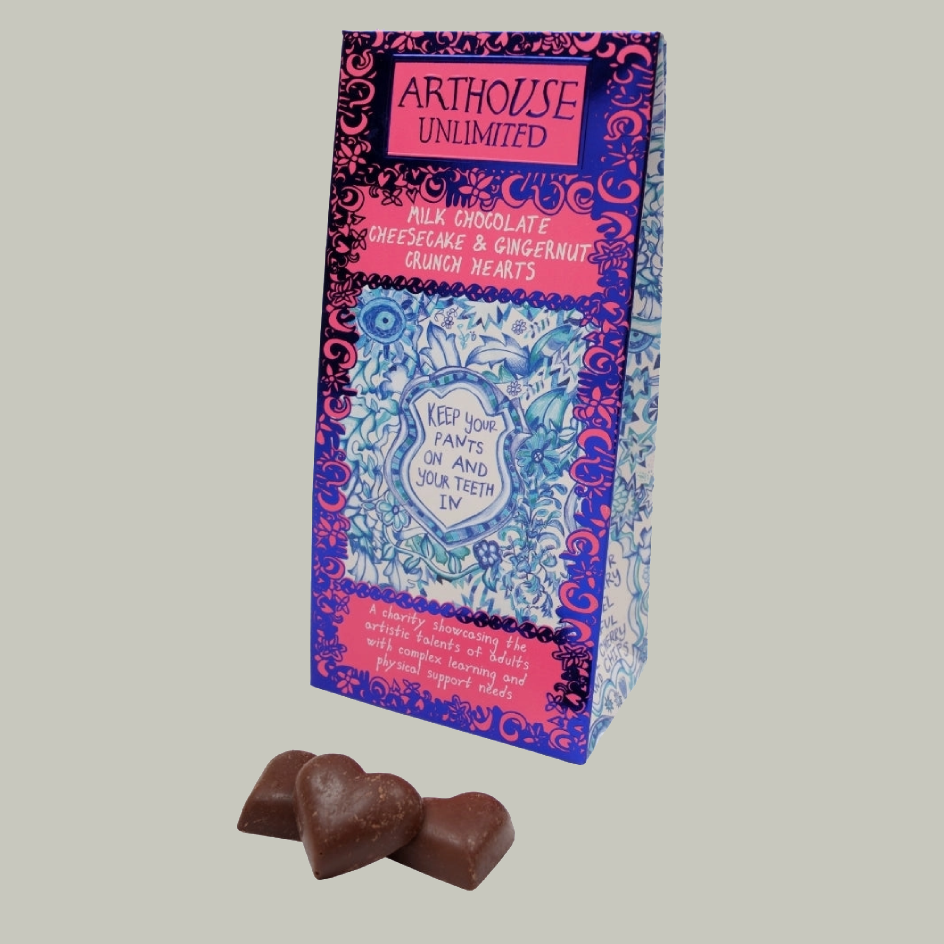 Blue and white patterned carton packaging with pink borders and the text 'ARTHOUSE UNLIMITED' and 'KEEP YOUR PANTS ON AND YOUR TEETH IN.' There are 3 chocolate hearts positioned in front of the box. The image has a biege background.