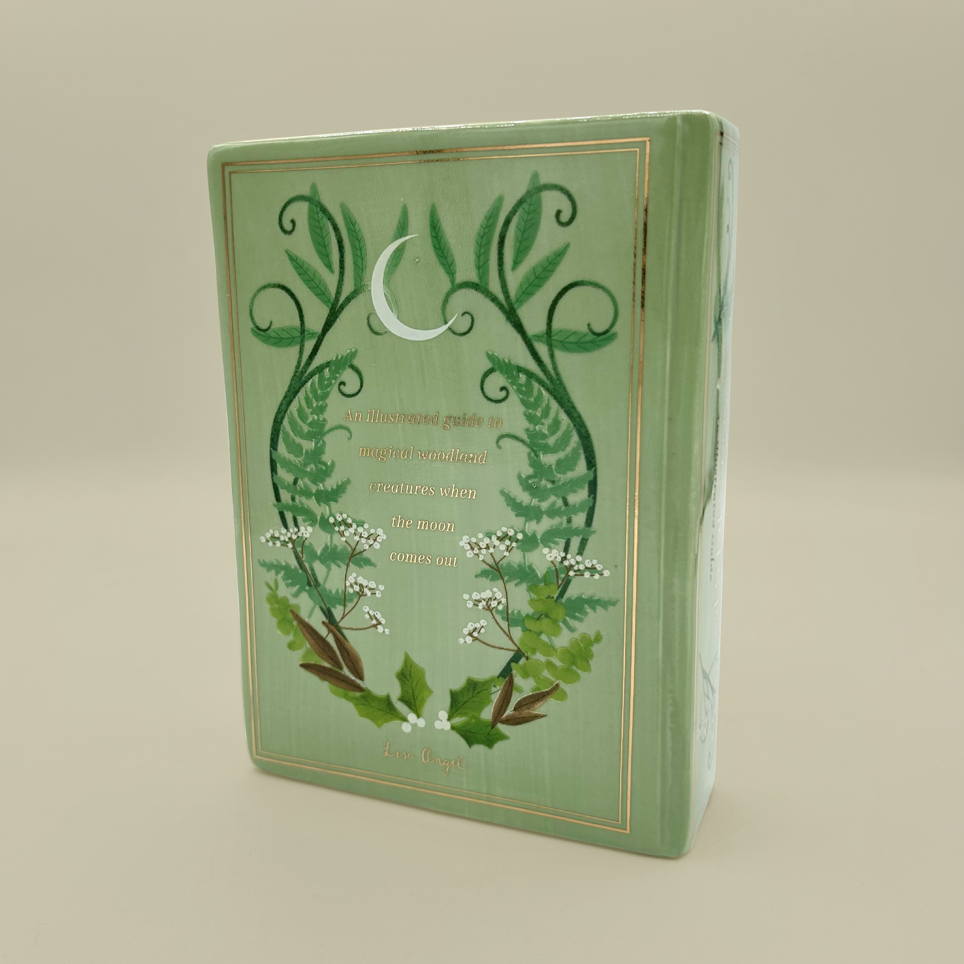 Green book shaped vase with floral design on a beige background
