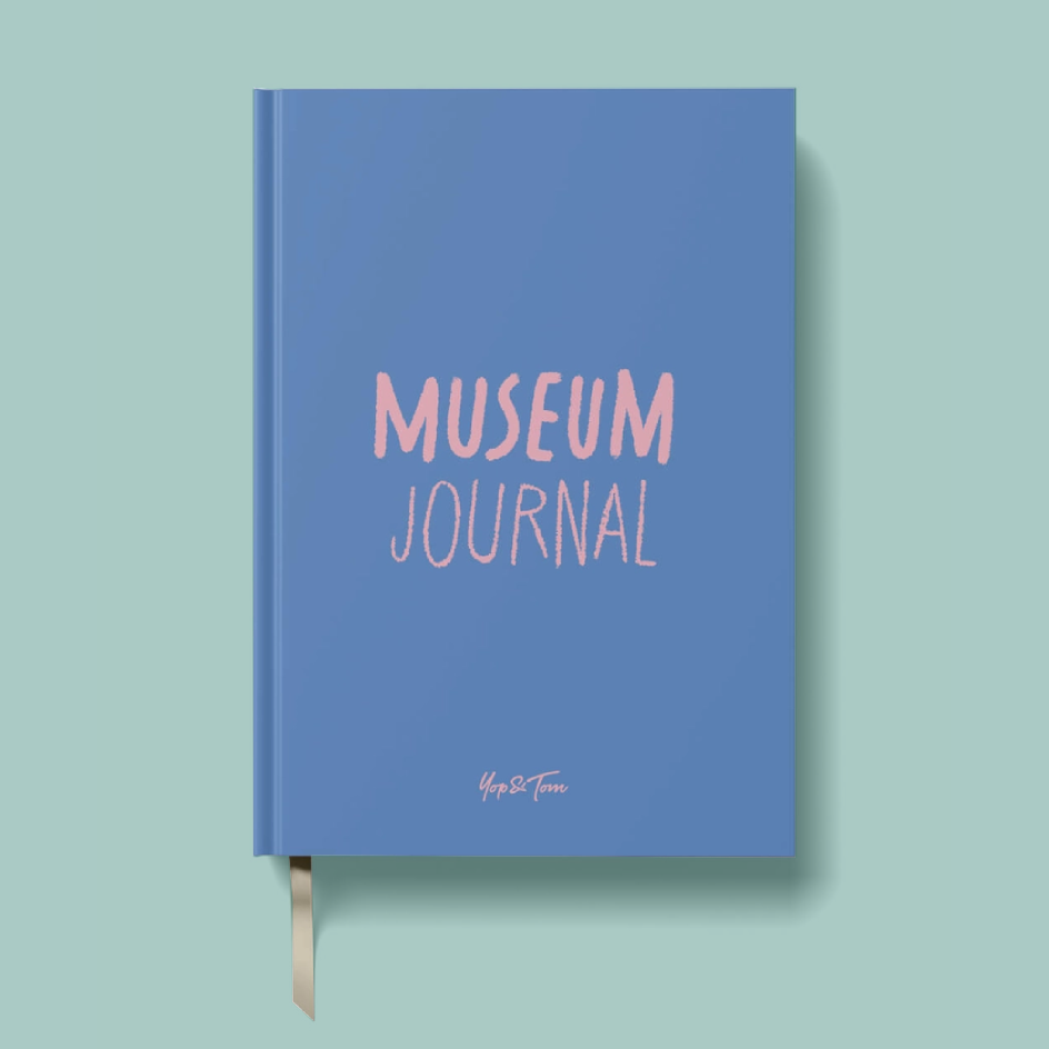 A blue hardcover journal with 'MUSEUM JOURNAL' printed in pink on the front cover, shown on a light mint green background with a ribbon bookmark hanging from the bottom.
