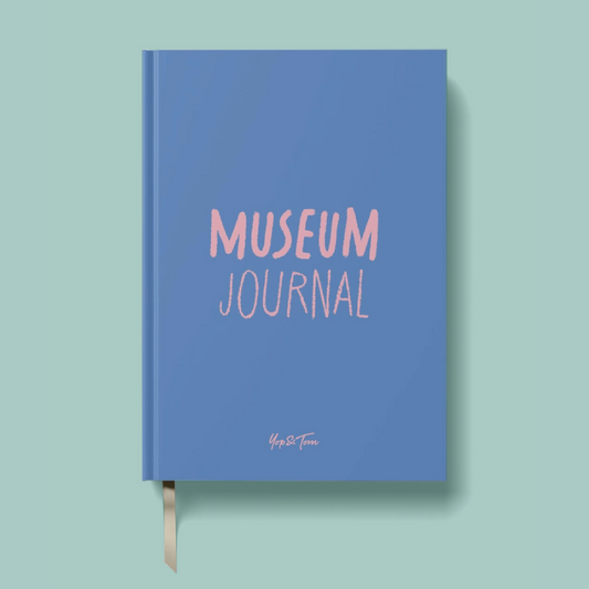 A blue hardcover journal with 'MUSEUM JOURNAL' printed in pink on the front cover, shown on a light mint green background with a ribbon bookmark hanging from the bottom.