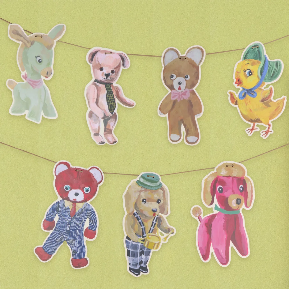 A set of colourful animal decorations hanging on string against a pale yellow-green background. The characters include a light green donkey, a pink bear wearing a green tie, a brown bear wearing a pink bow tie, a yellow chick with a green hat and blue scarf, a red bear in a blue striped suit, a tan bear in a green hat playing a drum, and a pink dog.