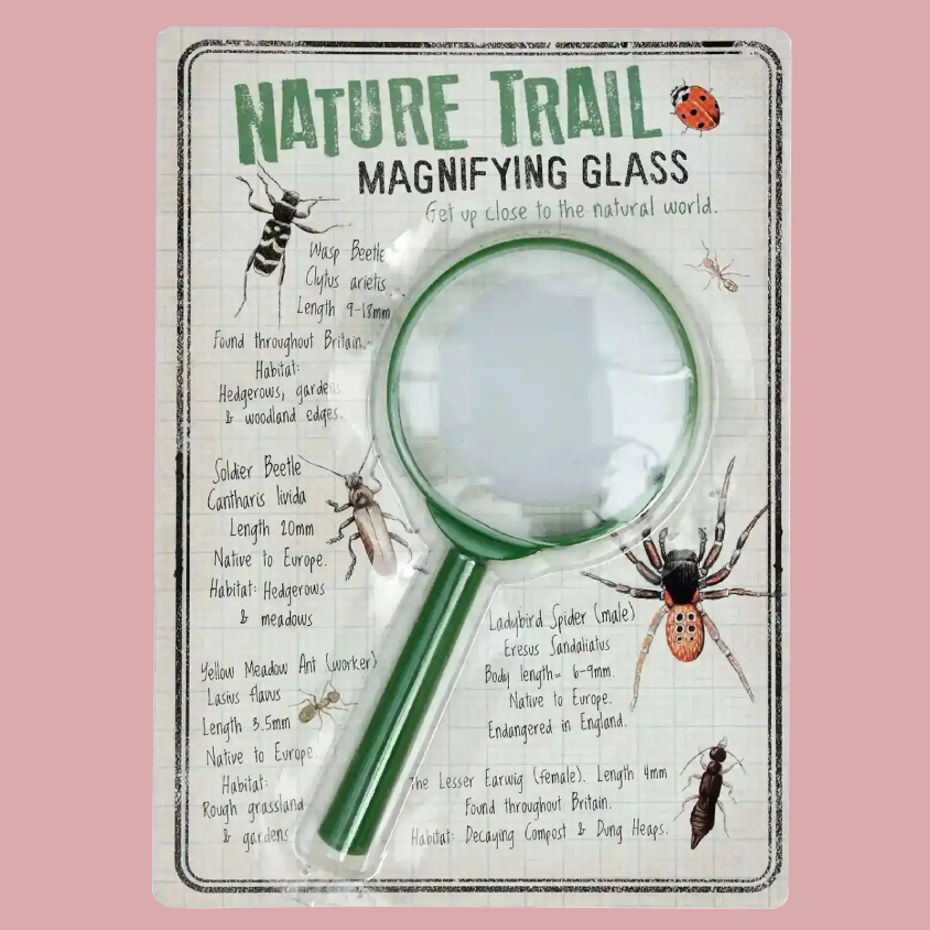 A packaged children's nature magnifying glass set against a solid pink background. The product is mounted on a white cardboard backing featuring educational text and illustrations of insects and spiders.