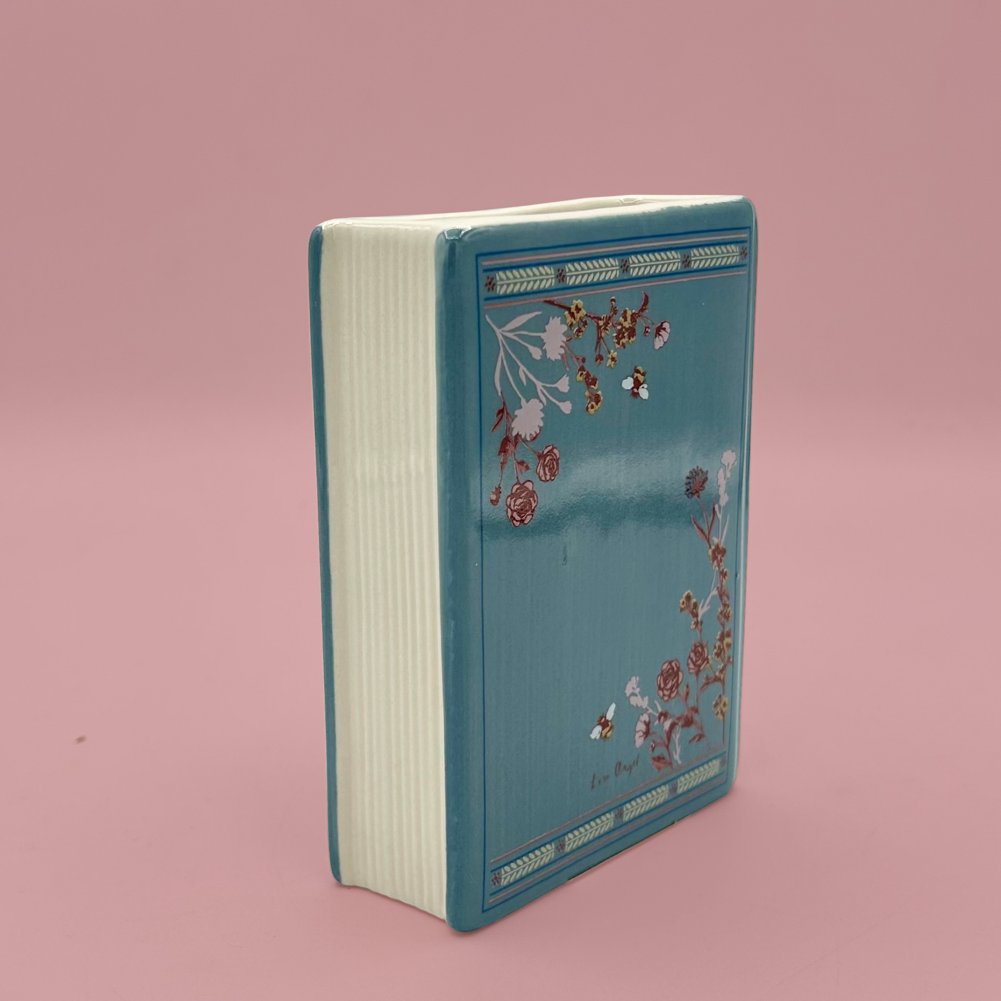 Blue book shaped vase with floral design on a pink background