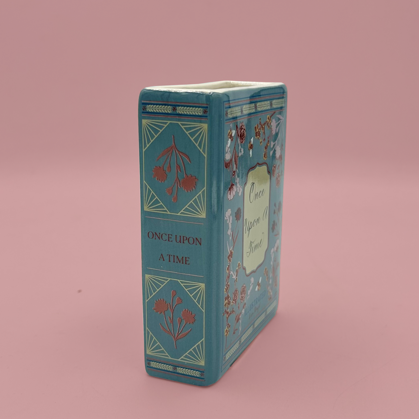 Decorative book-shaped vase with floral design on a pink background