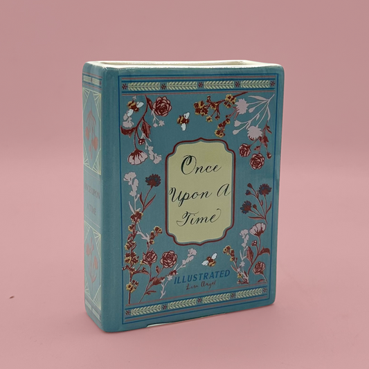 Blue book shaped vase with floral design and 'Once Upon A Time' text on a pink background