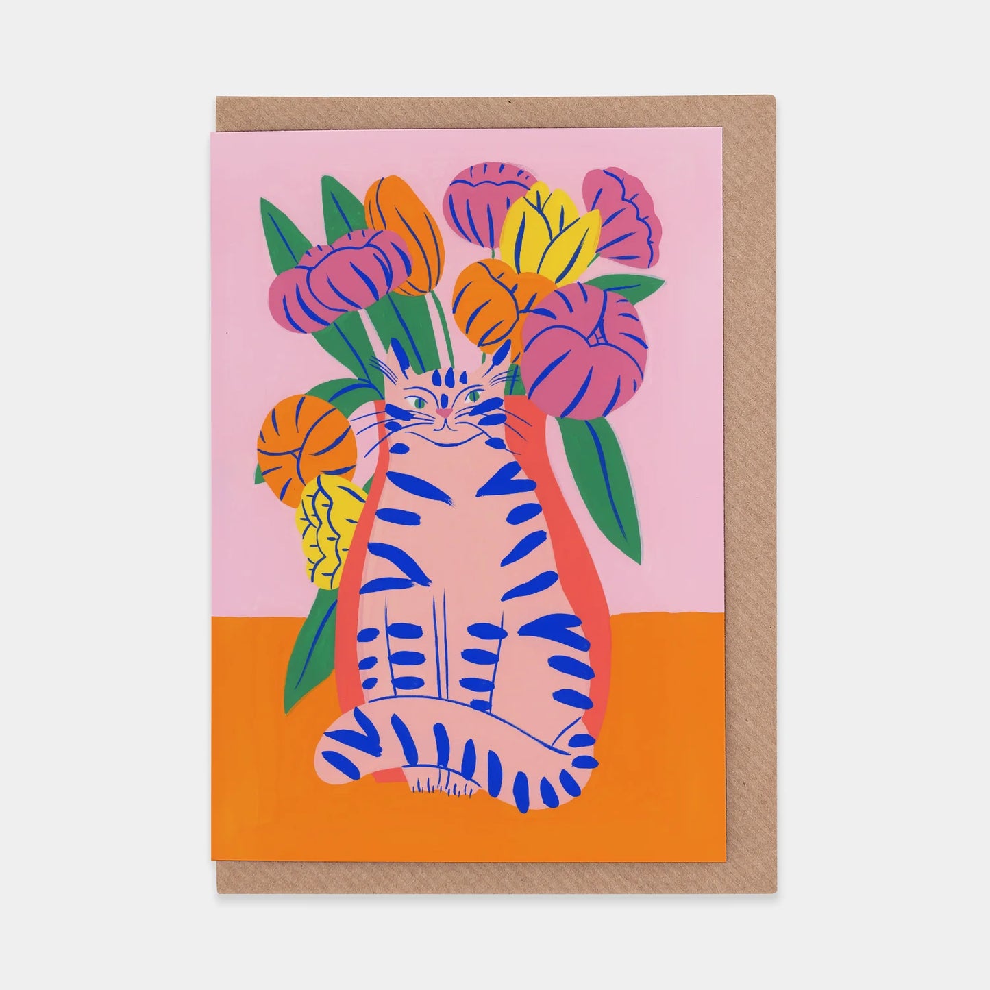 A portrait orientation greetings card with a digital illustration of a pink cat in front of pink, yellow, and orange flowers on a pink and orange background. The card is on a brown envelope on a plain backdrop. 
