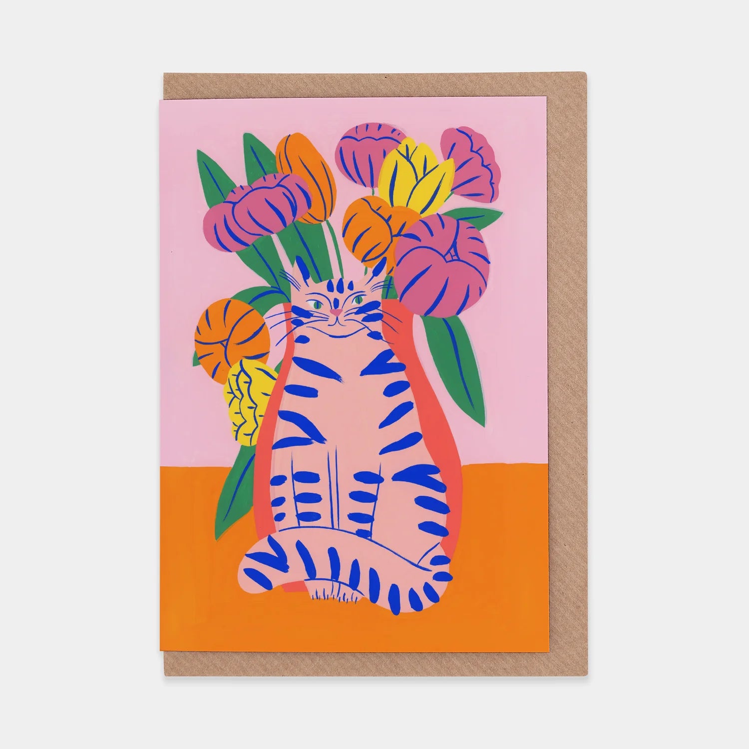 A portrait orientation greetings card with a digital illustration of a pink cat in front of pink, yellow, and orange flowers on a pink and orange background. The card is on a brown envelope on a plain backdrop. 