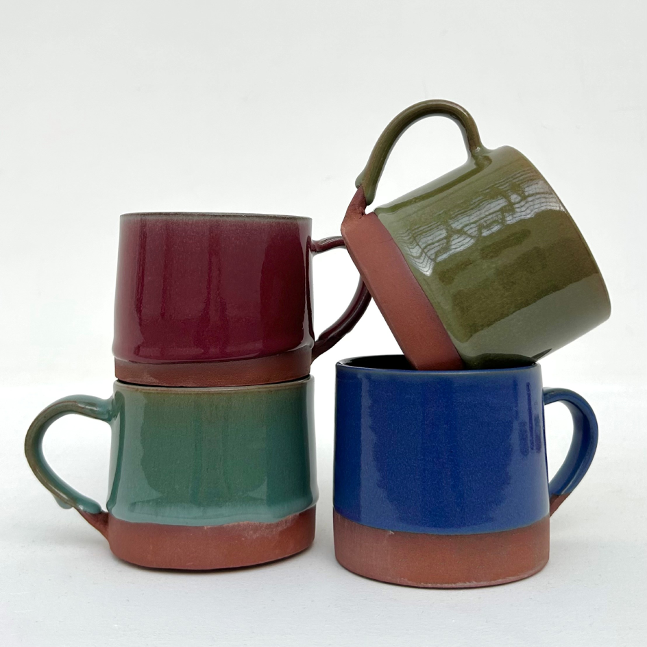 4 ceramic mugs in teal, green, blue, and nurgundy glazes stacked 2 by 2 on top of one another. The mugs are on a white background.