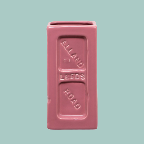 Pink brick-shaped vase with 'leeds' embossing on a teal background.