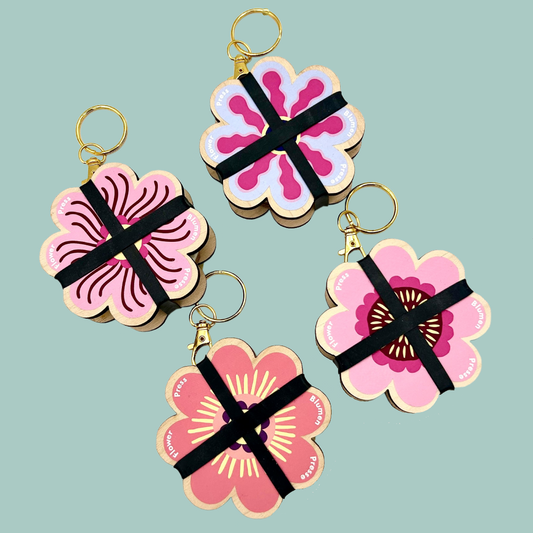Four pink flower shaped flower presses with gold keychains on a blue background. 