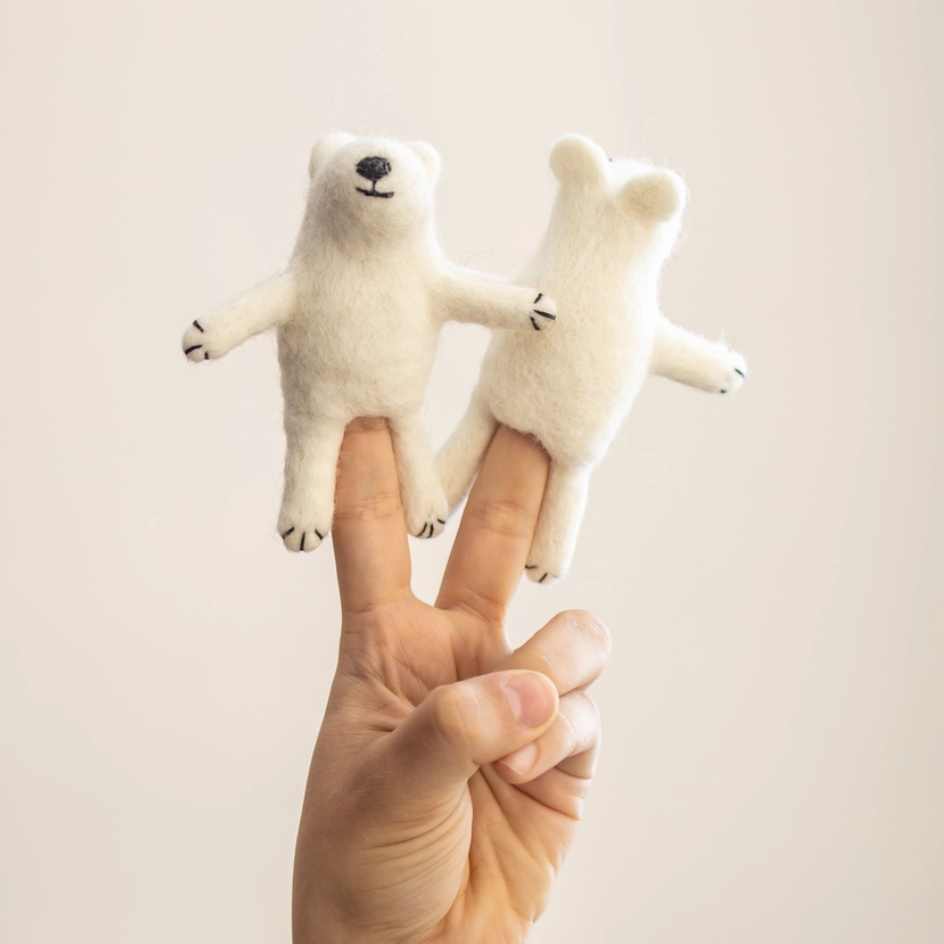 Two small felted white polar bear finger puppets with black embroidered facial features and paws, displayed on a person's fingers against a plain light beige background.