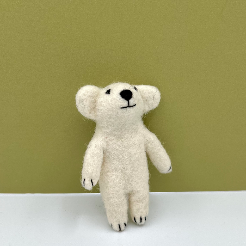 A small felted wool polar bear toy standing upright on a white surface against an olive green background.