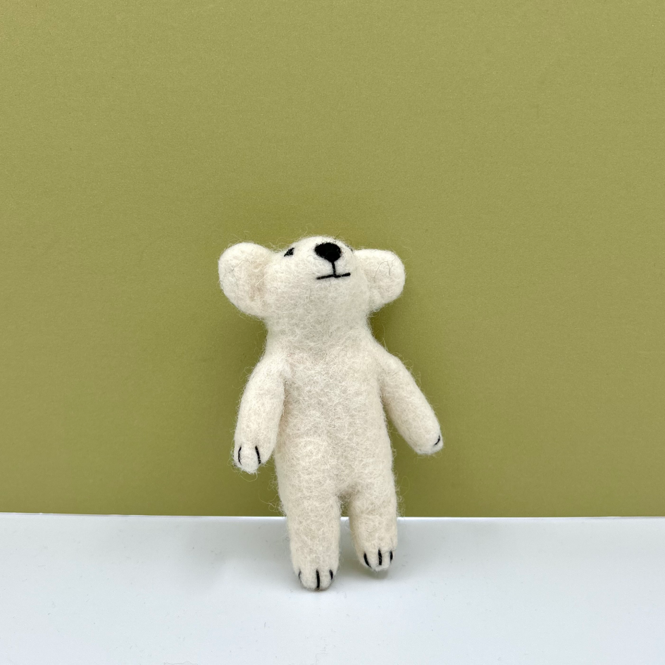 A small felted wool polar bear in off-white with black embroidered facial features and paws, standing on a white surface against a solid olive green background.