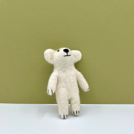 A small felted wool polar bear in off-white with black embroidered facial features and paws, standing on a white surface against a solid olive green background.