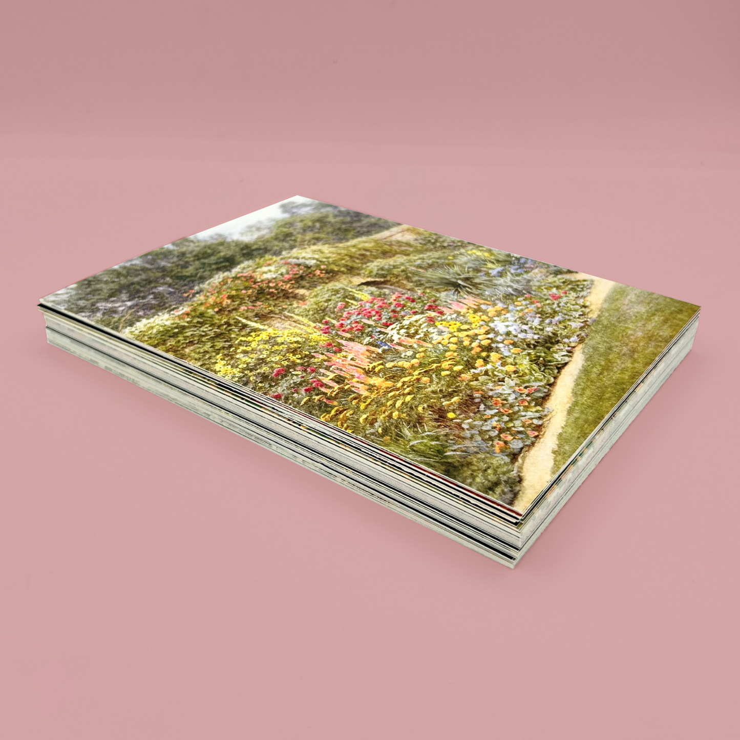 Stack of postcards, the top one features a garden scene. The stack is  on a pink background