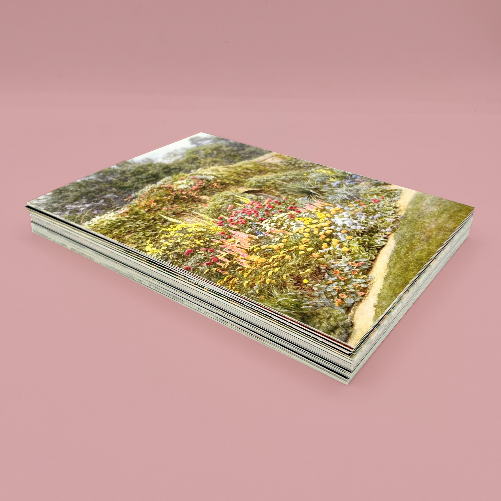 Stack of postcards, the top one features a garden scene. The stack is  on a pink background