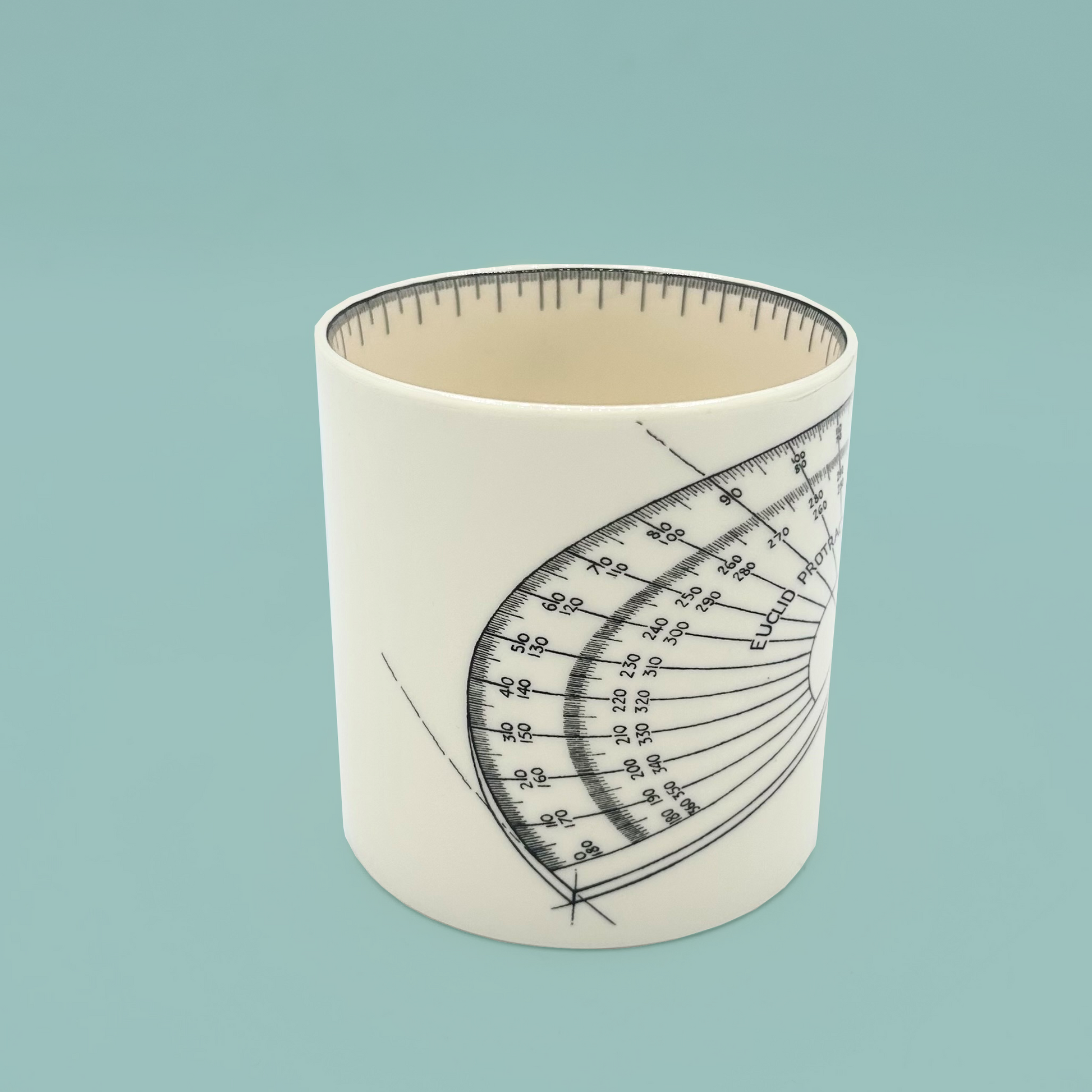 A cream mug with a technical drawing of a protractor. The mug is on a light teal background.