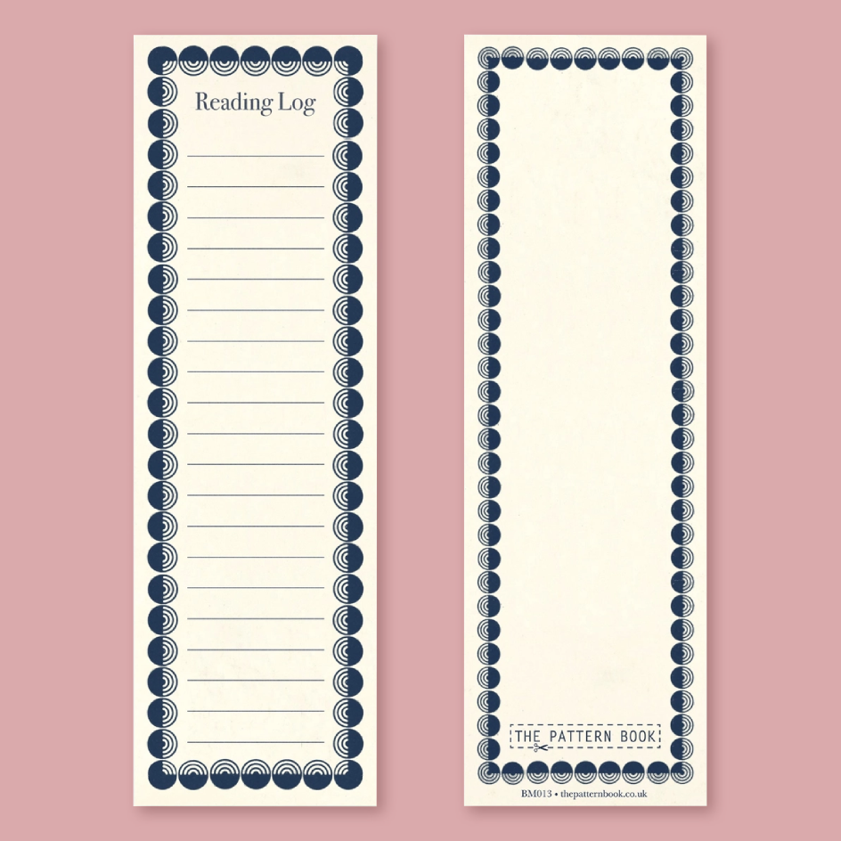 Two cream-colored bookmarks with navy decorative borders, shown on a dusty pink background. The left page is labeled 'Reading Log' with lined writing space, and the right page is blank with a decorative border.