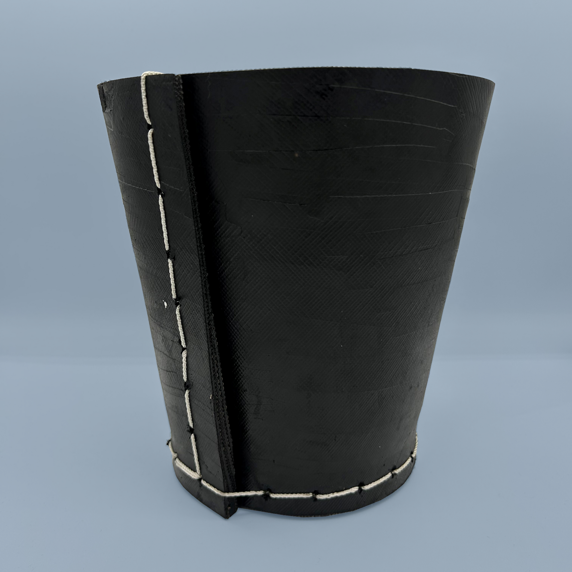 Black rubber plant pot with white stitching on a blue background