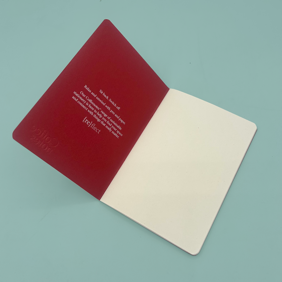 An open notebook or journal on a light blue background, showing a deep red left page with embossed branding and white text, and blank off-white pages on the right.