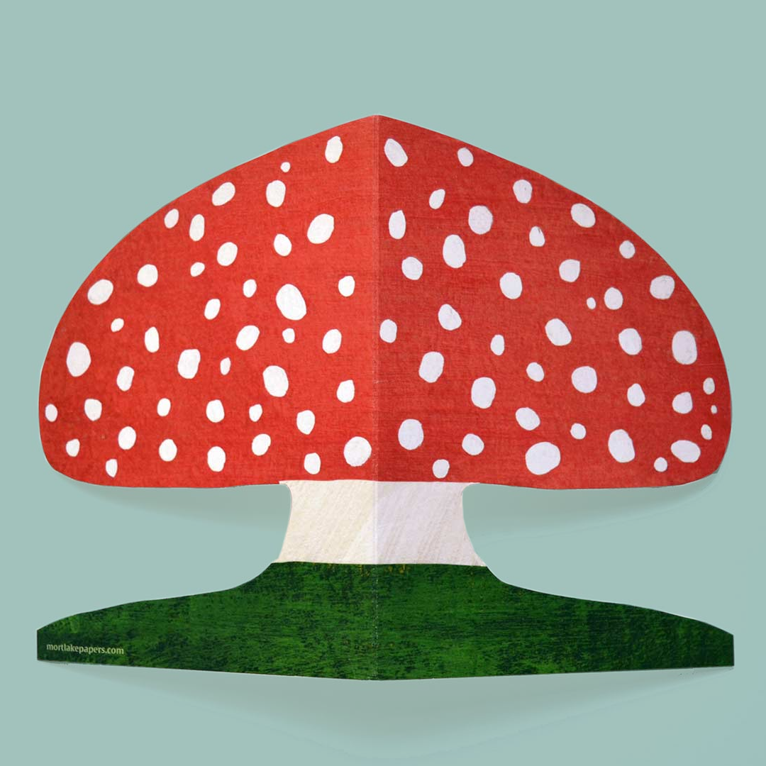 Red mushroom shaped greetings card with white spots on a green base against a light blue background