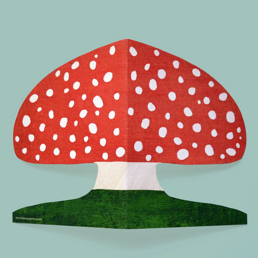 Red mushroom shaped greetings card with white spots on a green base against a light blue background