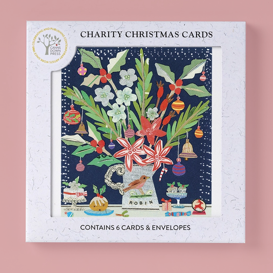 A boxed set of charity Christmas cards from Canns Down Press, featuring a white textured outer box with an illustrated festive floral and holiday scene on the front. The box is centered on a soft pink background, with text reading 'CHARITY CHRISTMAS CARDS' and 'CONTAINS 6 CARDS & ENVELOPES'.