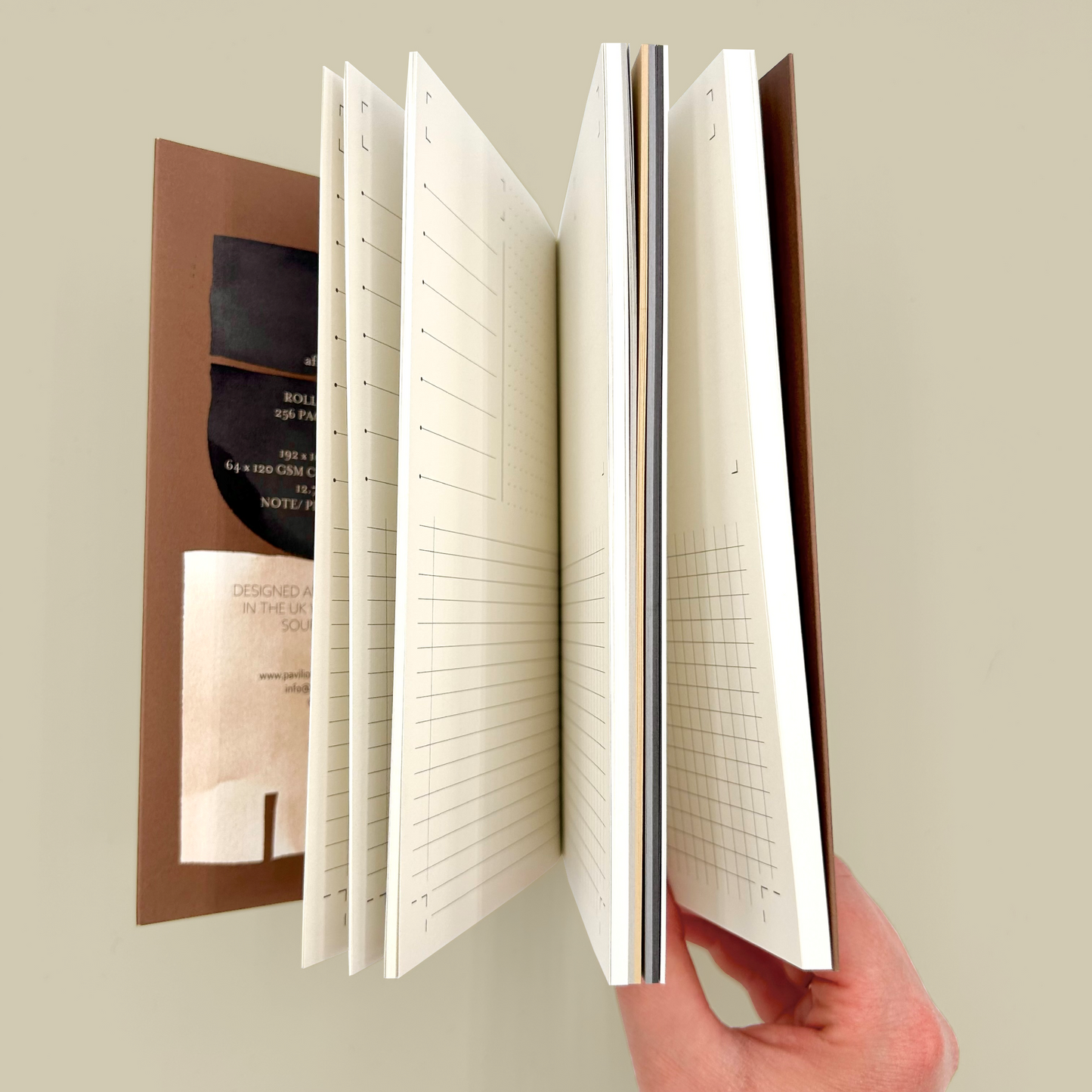 Hand holding a notebook with different page designs on a neutral background
