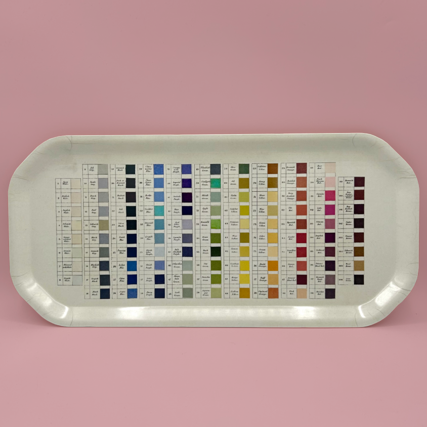 A rectangular colour chart tray with rounded corners, displaying multiple small color swatches arranged in columns with labels and numbers, set against a solid pink background.