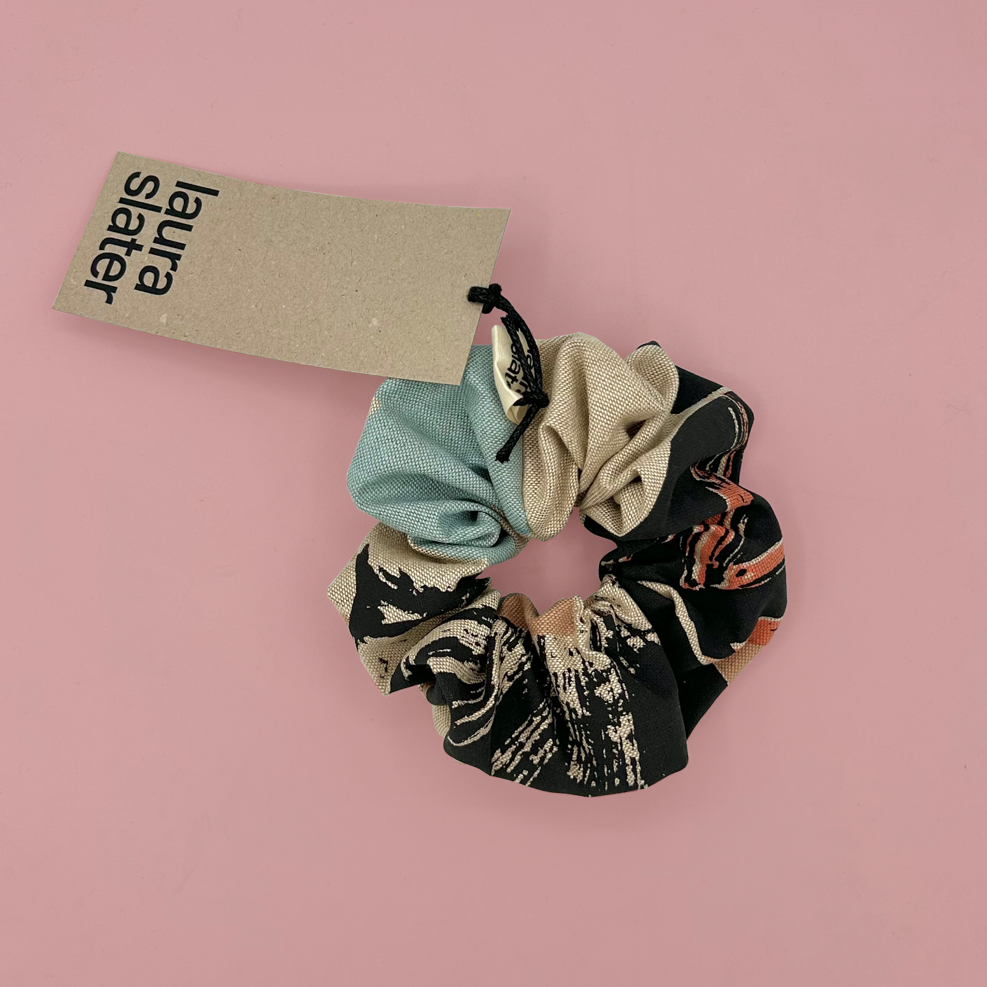 Patterned scrunchie with a 'Laura Slaterr' tag on a pink background