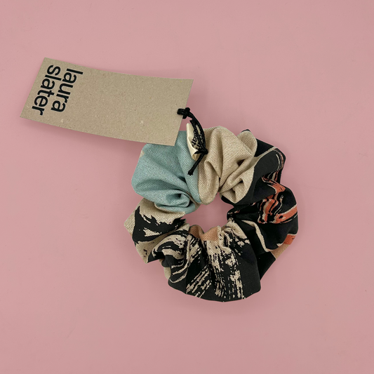 Patterned scrunchie with a 'Laura Slaterr' tag on a pink background