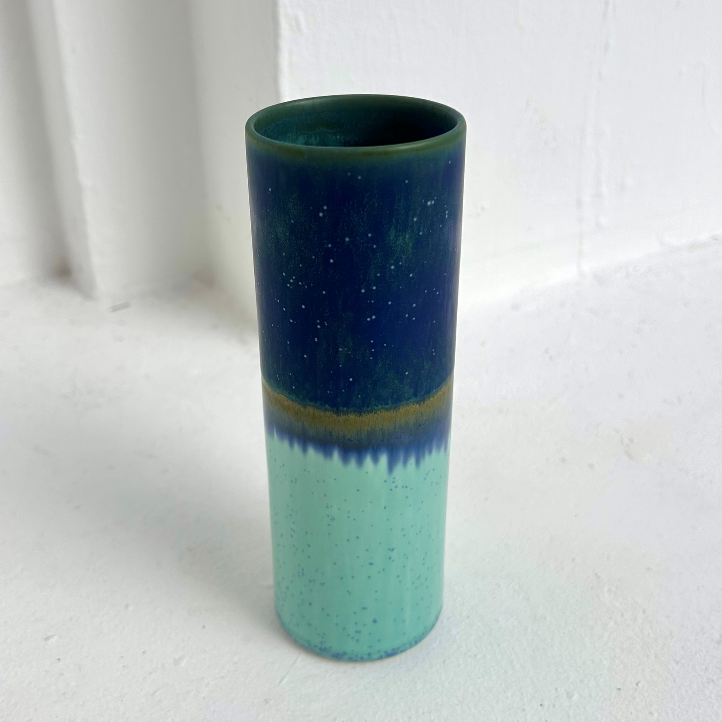 Cylindrical ceramic vase with two-tone green and blue gradient on a white background