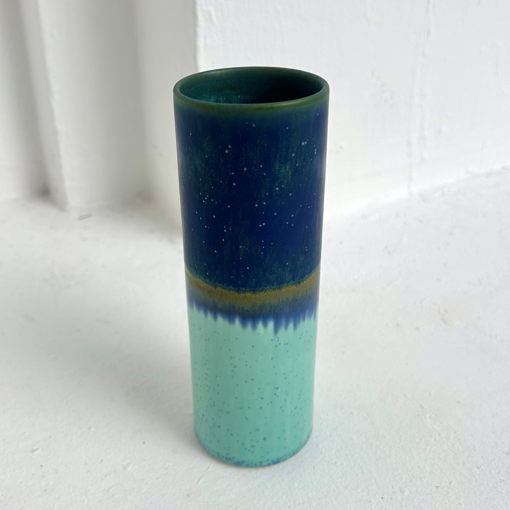 Cylindrical ceramic vase with two-tone green and blue gradient on a white background