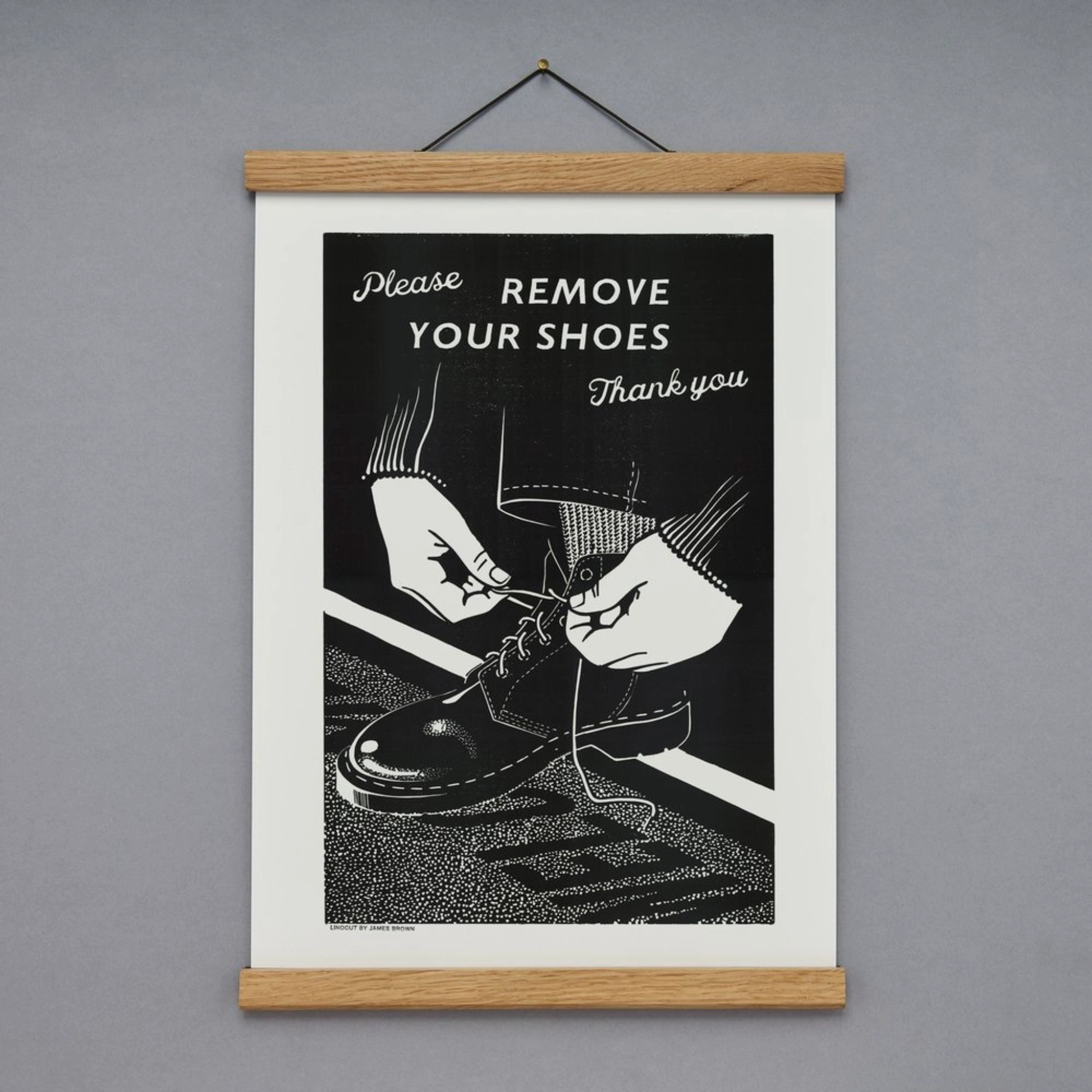 Framed poster with a black and white illustration of hands untying shoes and text 'Please Remove Your Shoes Thank you' on a gray background.
