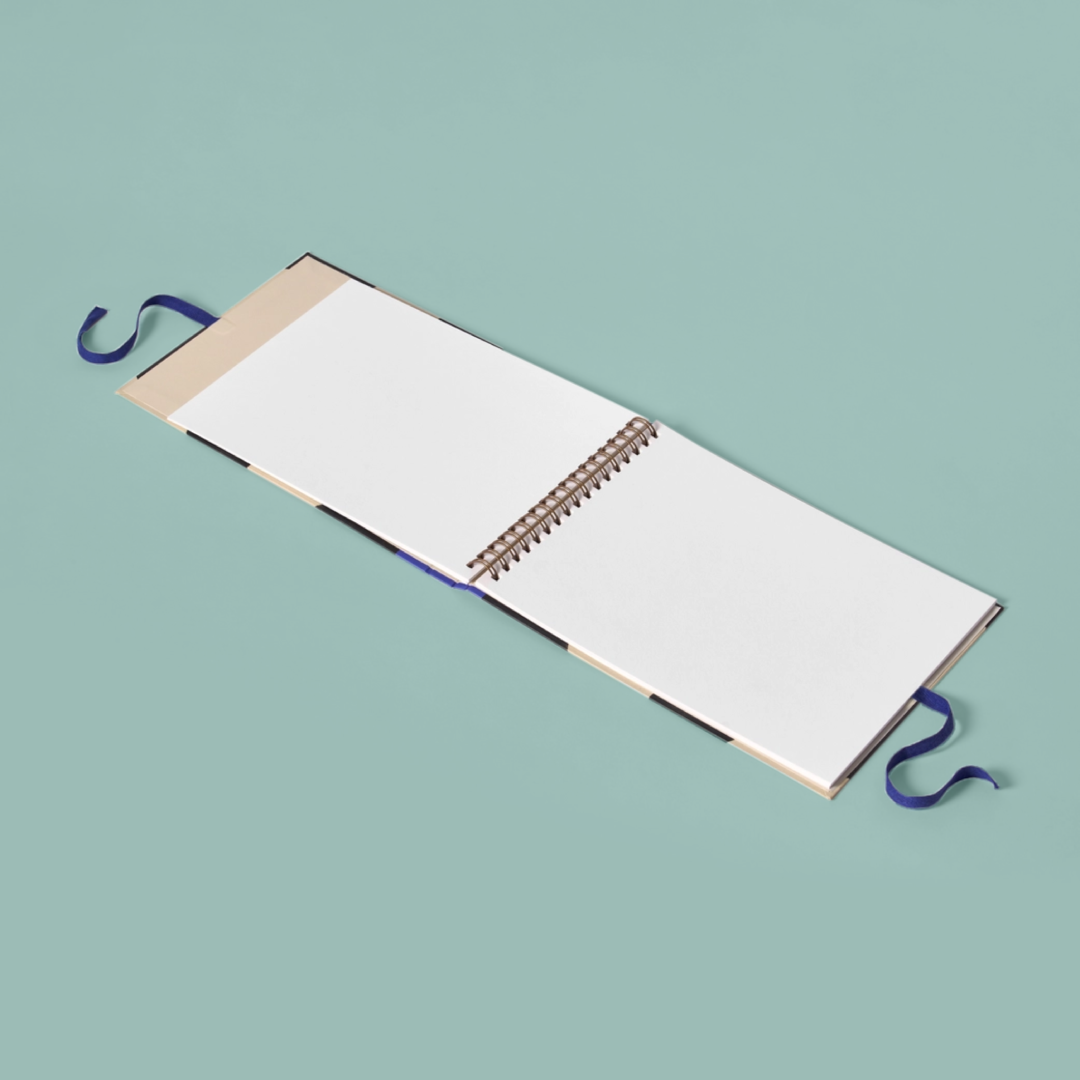 Open notebook with spiral binding and blue ribbon closure, on a teal background.