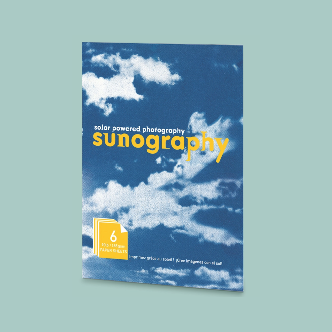 Solar powered photography cyanotype kit with a blue cloudy background and yellow text. The kit is on a teal background. 