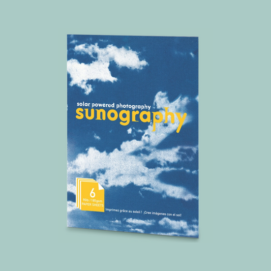 Solar powered photography cyanotype kit with a blue cloudy background and yellow text. The kit is on a teal background. 