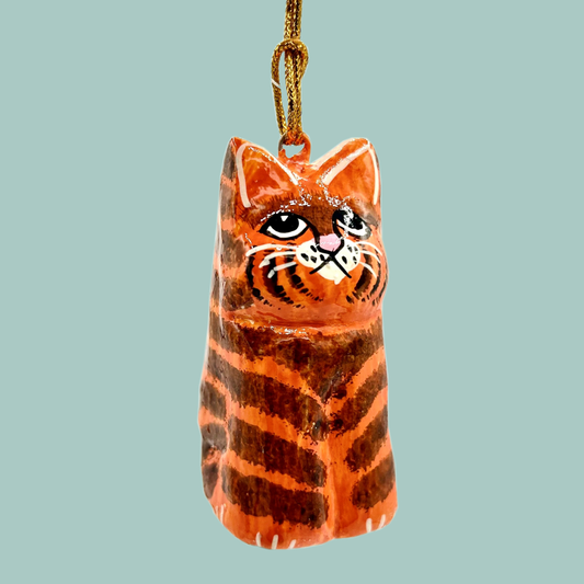 Cat shaped ornament painted with orange and brown stripes, hanging on a gold string and on a blue background.