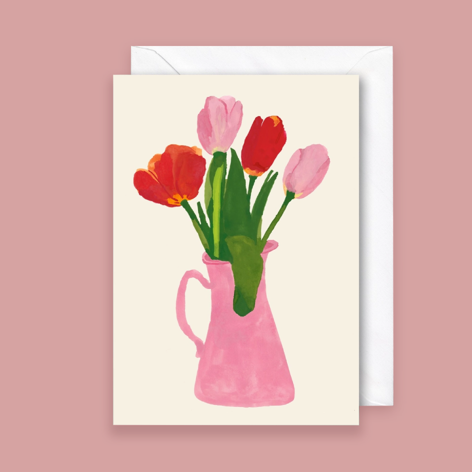 A greeting card with a watercolor-style illustration of tulips in a pink pitcher, shown with a white envelope against a dusty pink background.