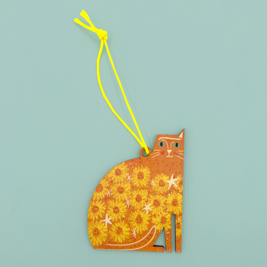 Orange cat shaped hanging ornament with flower and star embellishments and one ear. The decoration is hanging from a neon yellow string. 