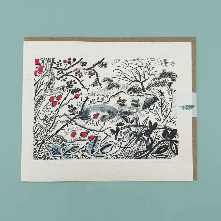 A greetings card featuring a black ink botanical and animal illustration with red berries and blue-gray accents, mounted on a kraft envelope against a muted teal background.