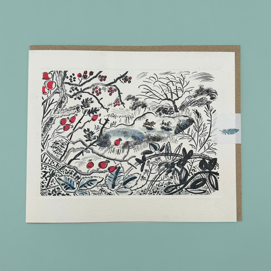 A greetings card featuring a black ink botanical and animal illustration with red berries and blue-gray accents, mounted on a kraft envelope against a muted teal background.