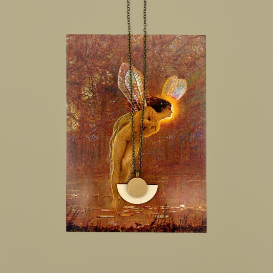 A cream and gold pendant on a brass coloured chain, sat atop a postcard of Atkinson Grimshaw's Iris painting.