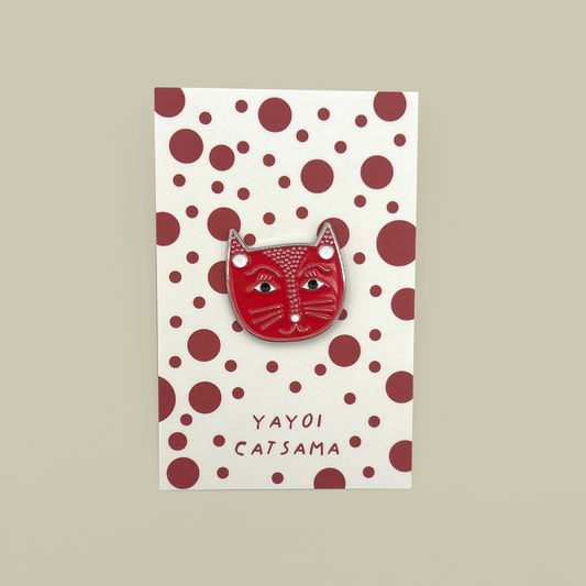A red cat-face enamel pin with white and black details, mounted on a cream card with dark red polka dots and the text 'YAYOI CATSAMA'.