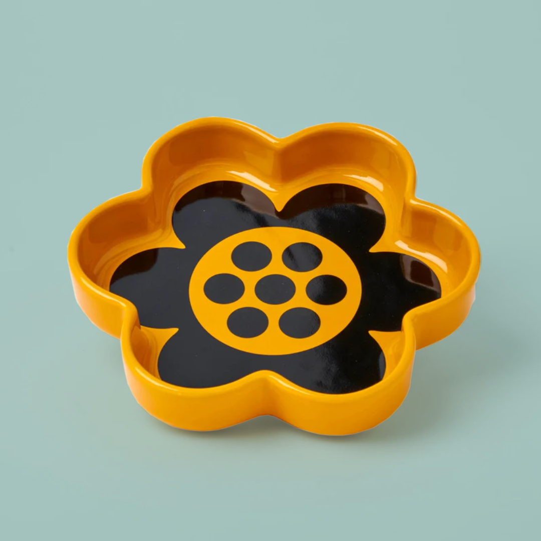 A yellow and black flower-shaped ceramic dish on a teal background.